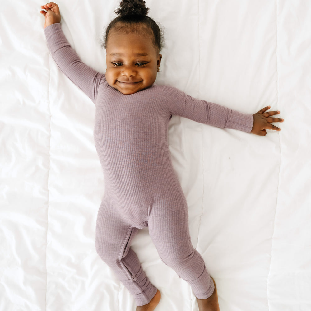 Child laying on a bed wearing a Heather Smokey Lavender ribbed crescent zippy