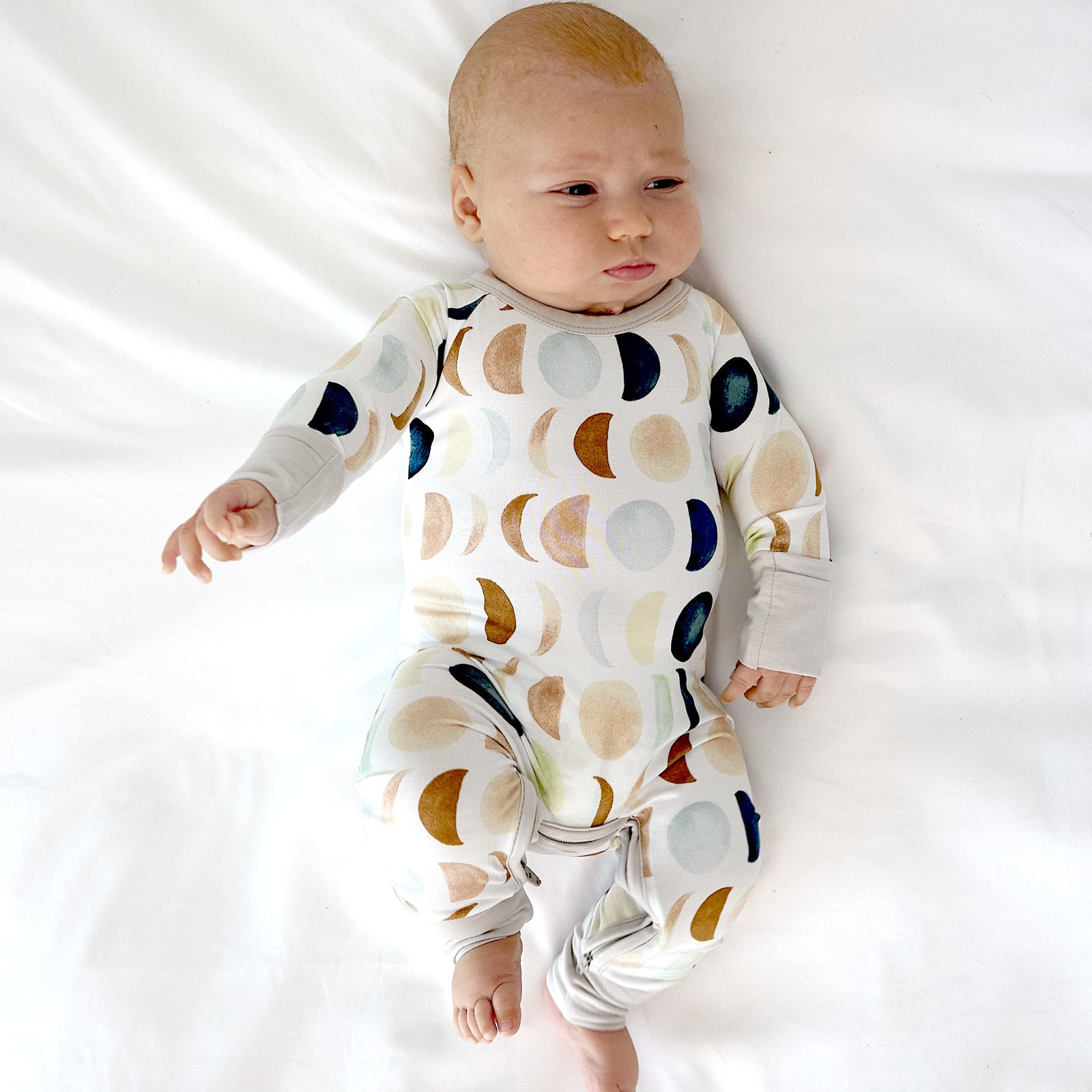 baby laying down wearing the crescent zippy in luna neutral