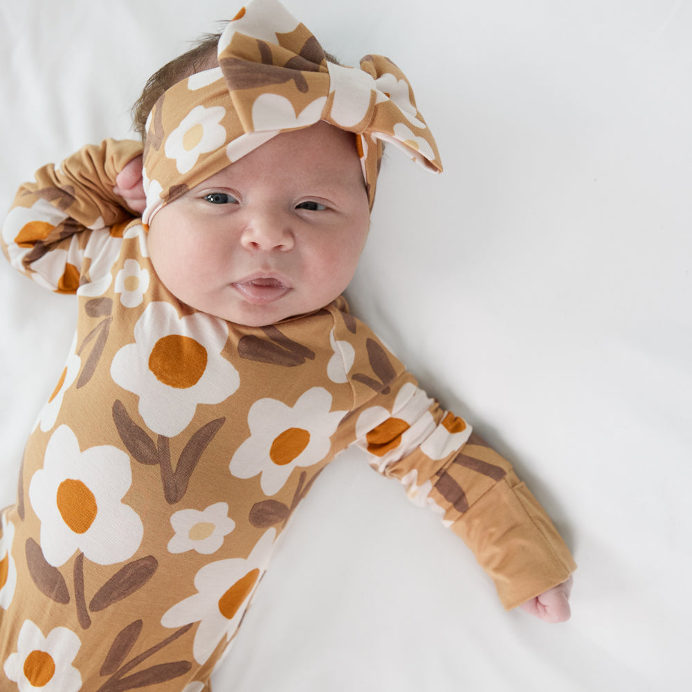 close up image of a child laying on a bed wearing a Daisy Daydream crescent zippy and matching luxe bow headband 