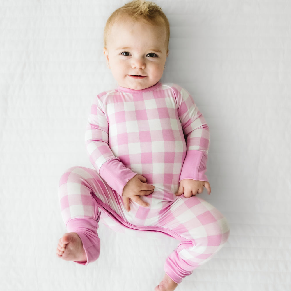 Click to see full screen - Child laying on a bed wearing a Pink Gingham crescent zippy