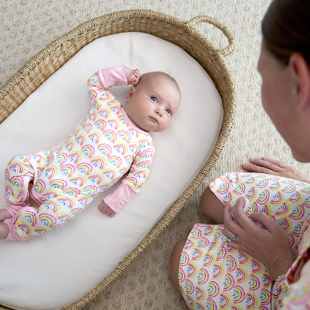 baby in basket wearing crescent zippy with mom watching over her