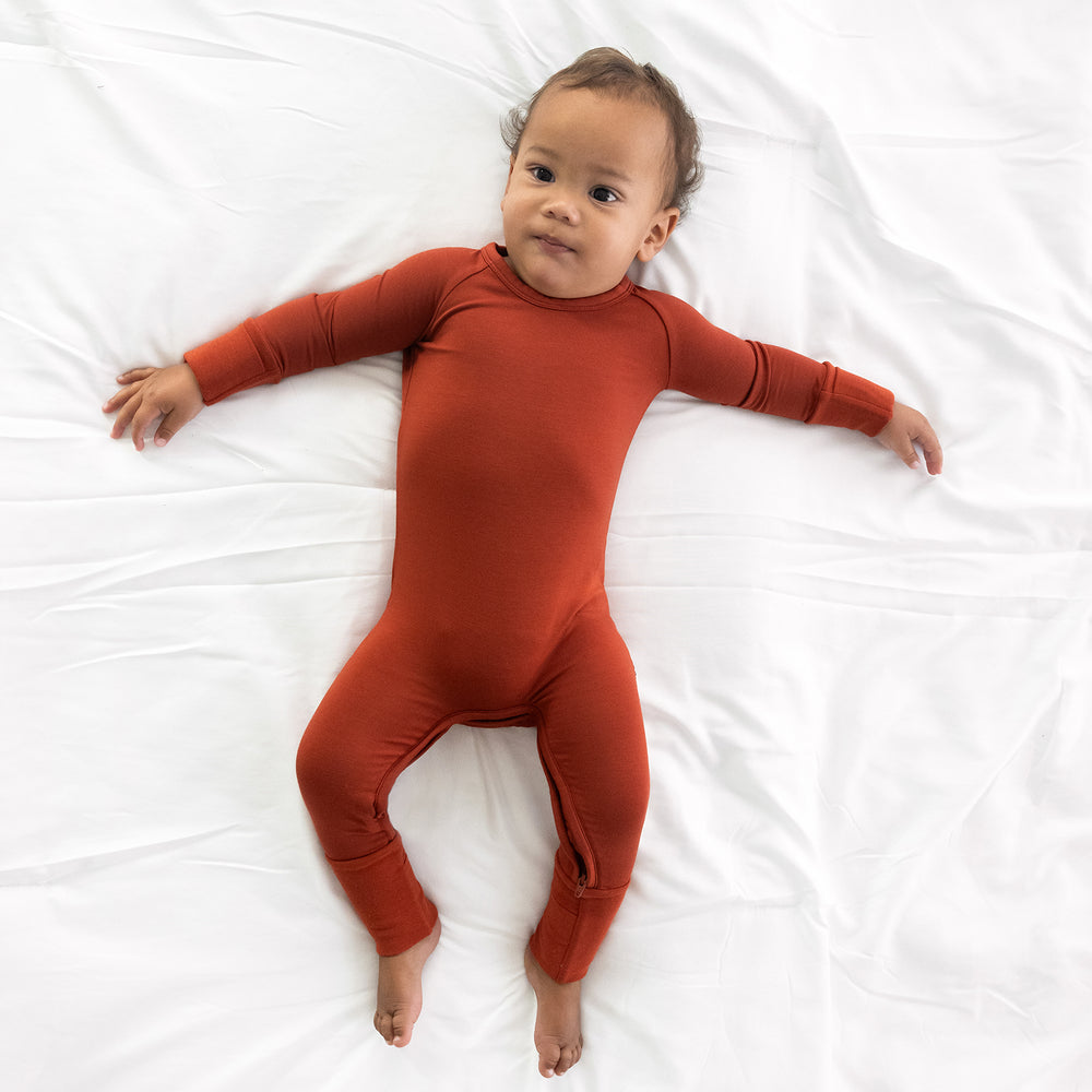 Child laying on a bed wearing a Cozy Rust crescent zippy