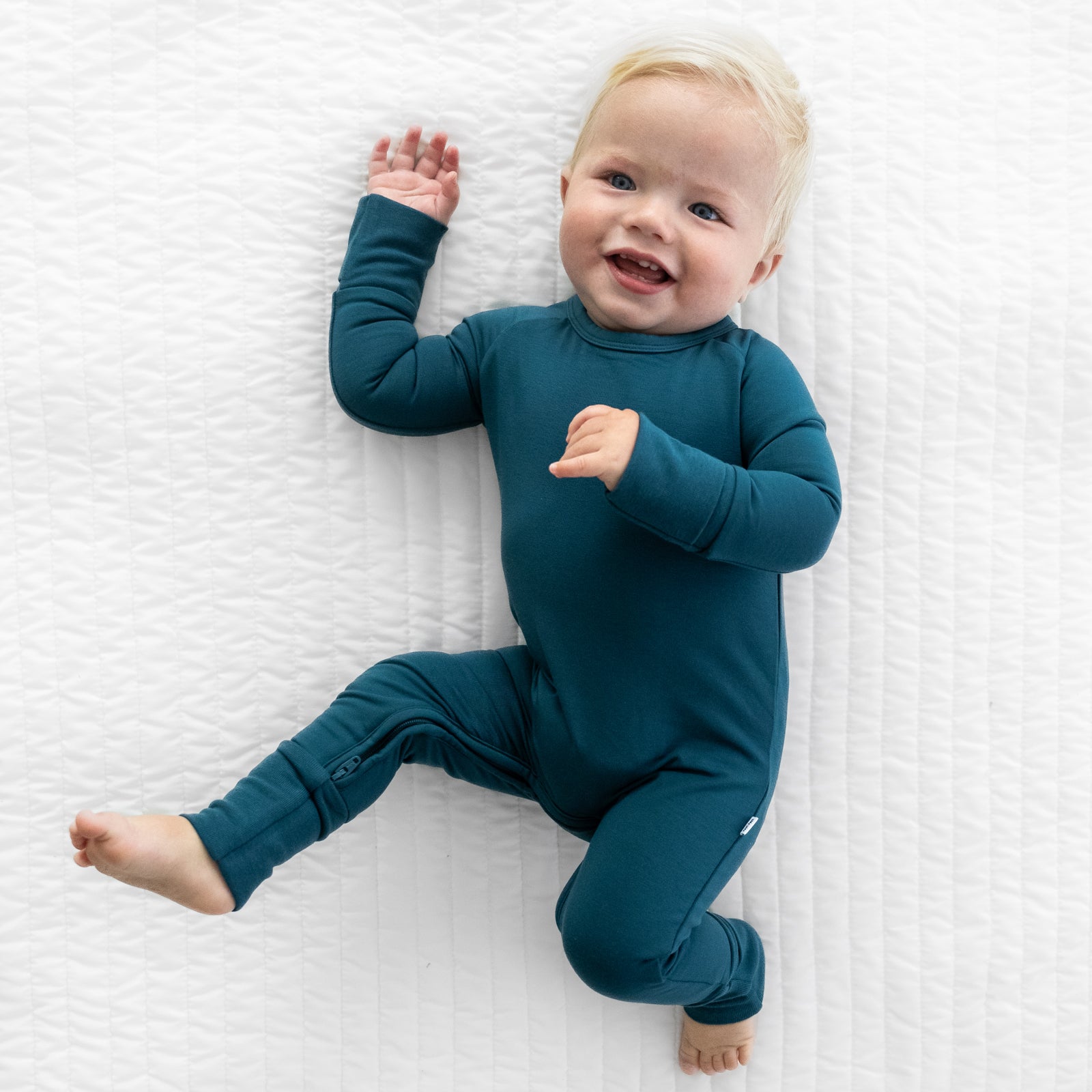 child laying on a bed wearing a Cozy Twilight Teal crescent zippy