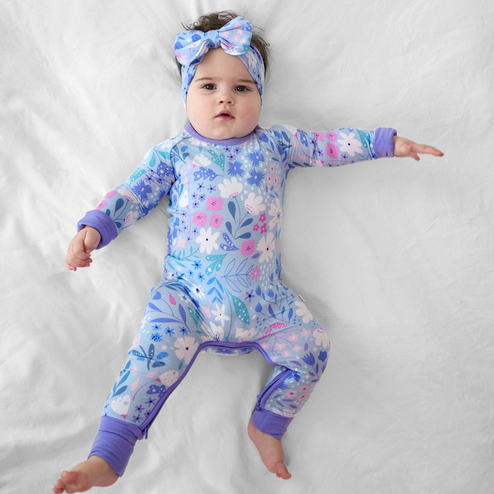 Child laying on a bed wearing a Magical Meadow crescent zippy paired with a matching luxe bow headband