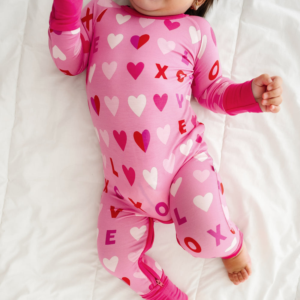 Click to see full screen - Alternate image of a child laying on a bed wearing a Pink XOXO crescent zippy showing off the leg zipper
