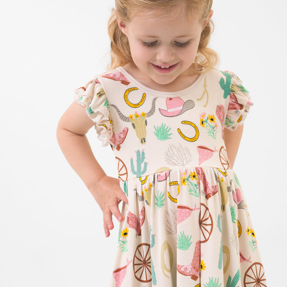 Close up image of a child posing wearing a Pink Ready to Rodeo twirl dress detailing the flutter sleeves