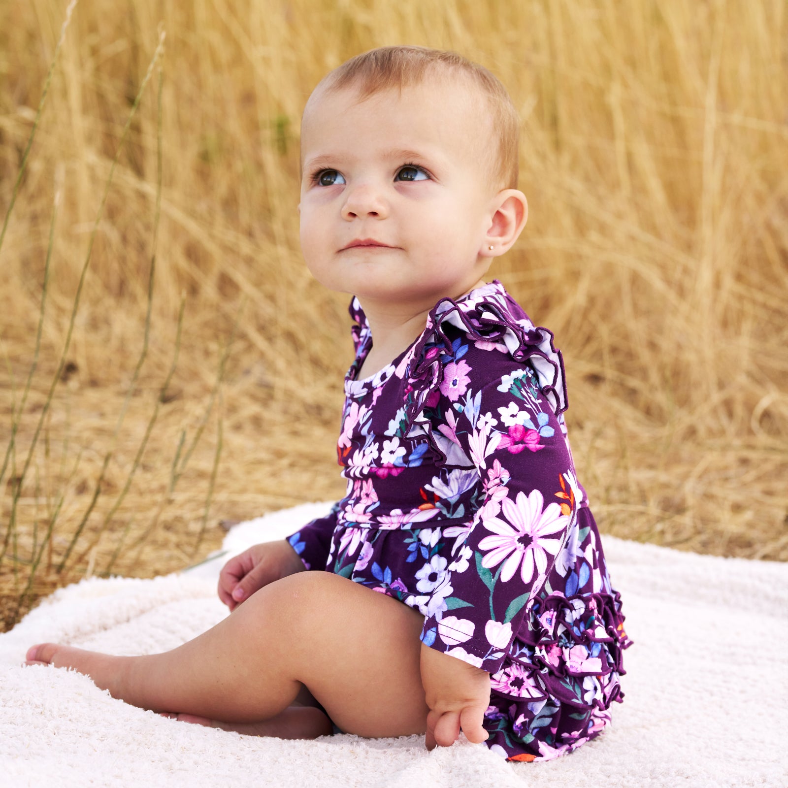 Girl sitting outdoors on a white blanket while wearing the Violet Meadow Bubble Romper