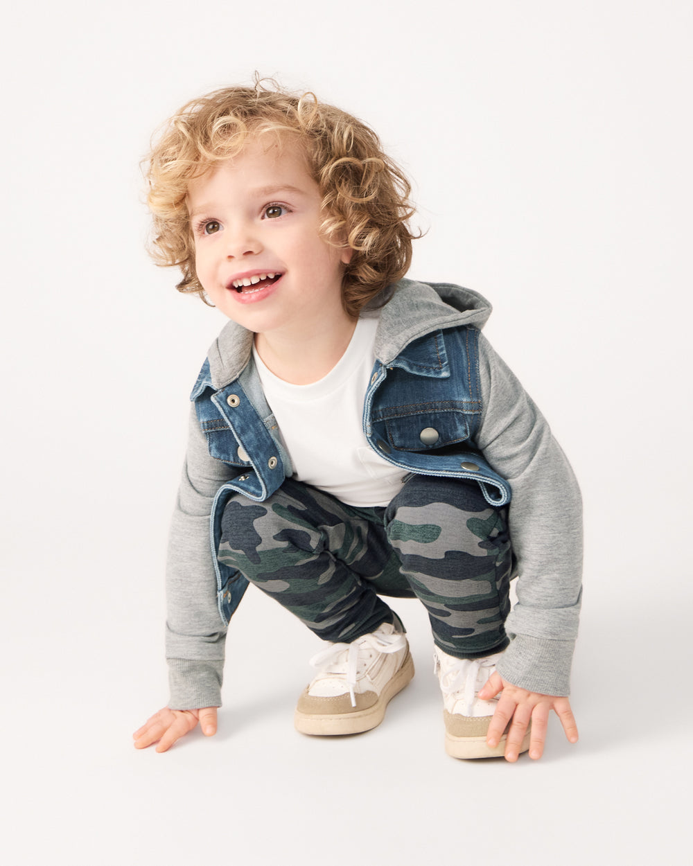 Crouching boy wearing the Vintage Camo Jogger with a hooded denim jacket