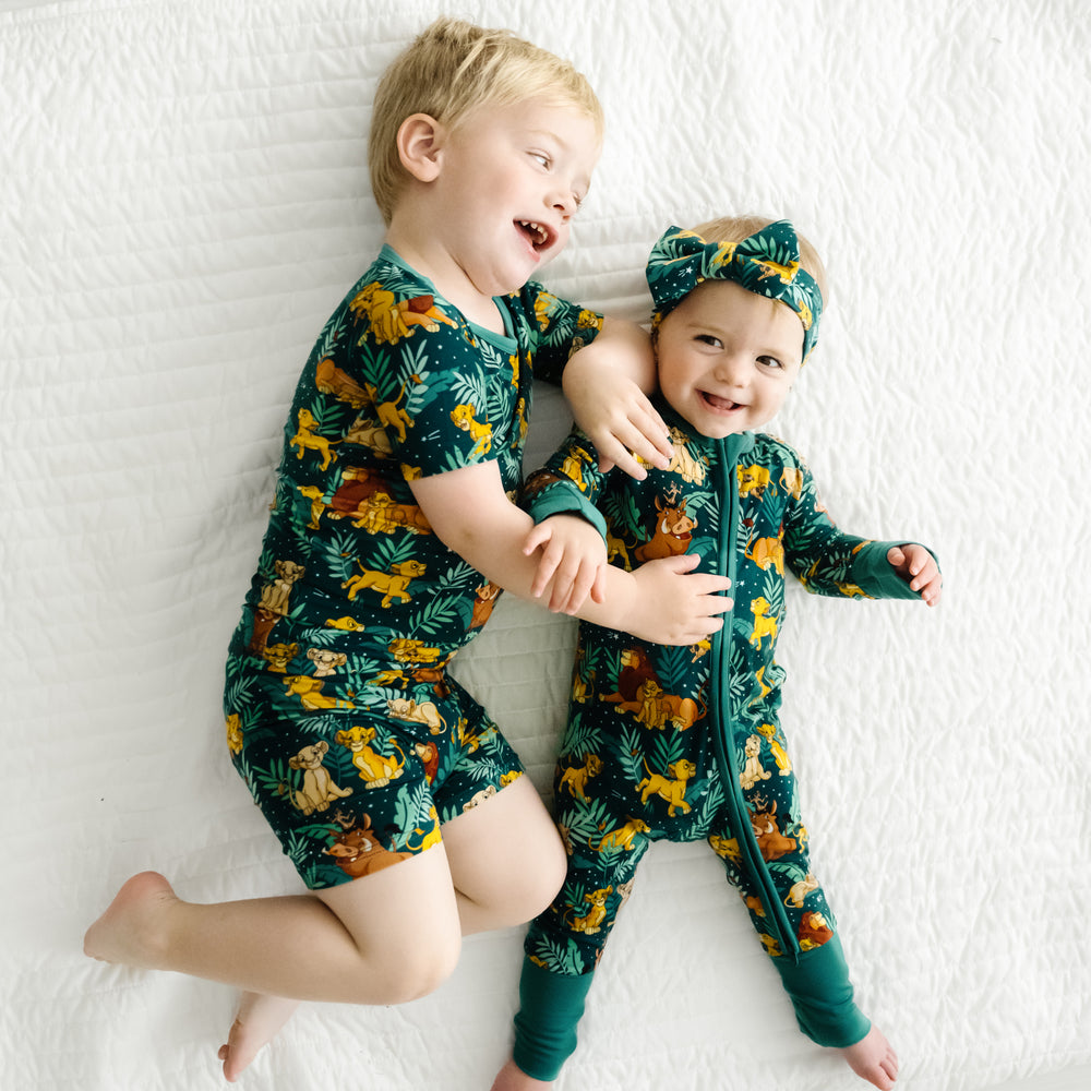 Two children laying on a bed wearing Disney Simba's Sky pajamas and matching luxe bow headband