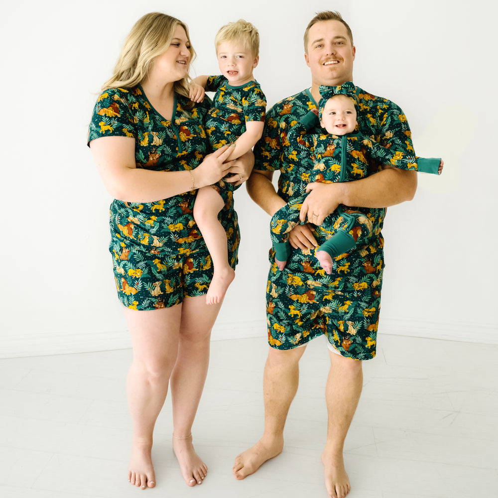 Family of four wearing matching Disney Simba's Sky pajama pants. Dad is wearing men's Disney Simba's Sky men's pajama shorts paired with a matching men's pajama top. Mom is wearing Disney Simba's Sky women's pajama top and matching pajama shorts. Their children are wearing matching pjs in zippy and two piece styles