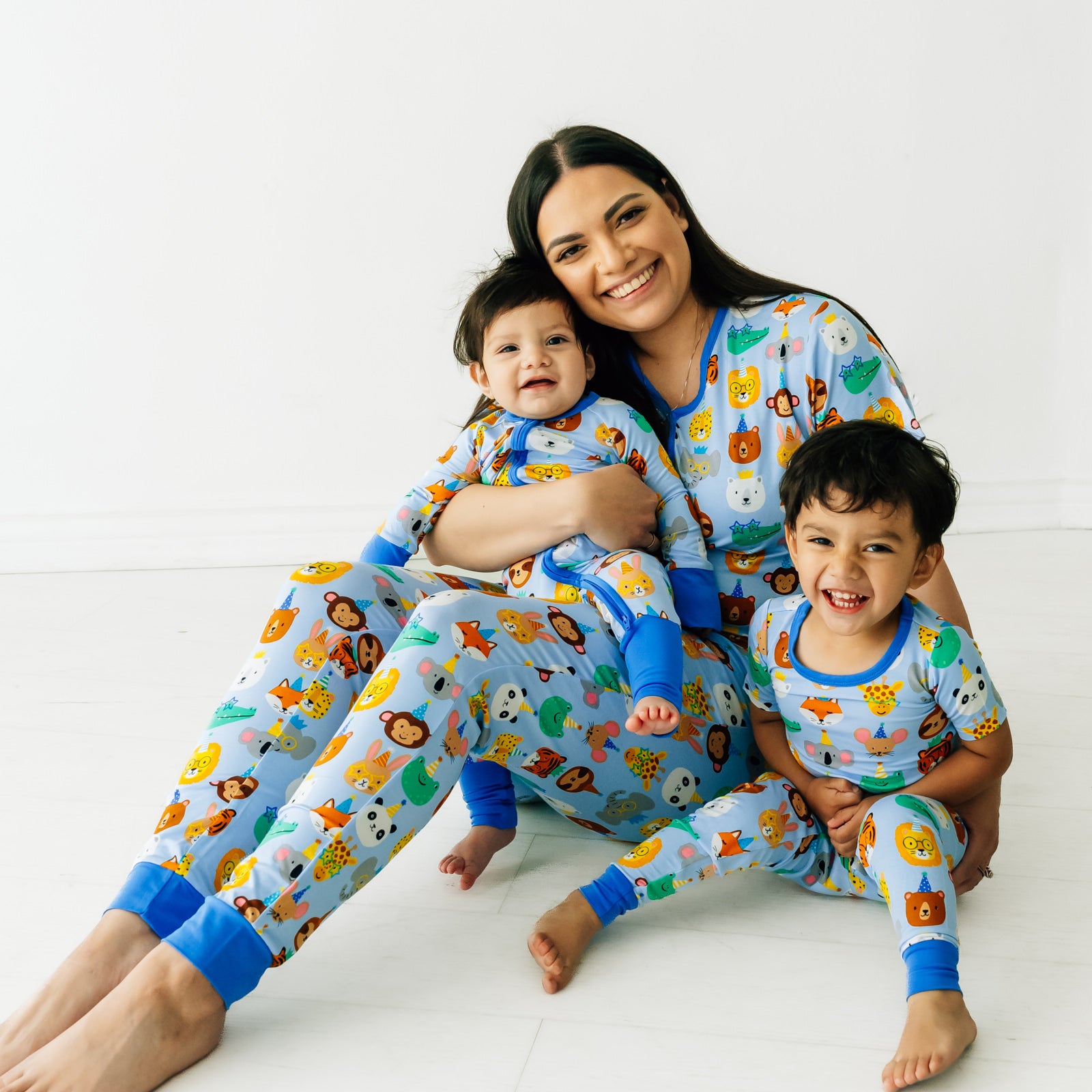 Woman and her two children sitting and posing. Woman is wearing women's Blue Party Pals pj top and matching women's pj pants. Kids are wearing matching Blue Party Pals pjs in zippy and two piece styles.