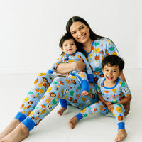 Woman and her two children sitting and posing. Woman is wearing women's Blue Party Pals pj top and matching women's pj pants. Kids are wearing matching Blue Party Pals pjs in zippy and two piece styles.
