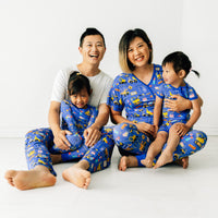 Family of four wearing matching Birthday Builder pjs. Dad is wearing men's Birthday Builders men's pj pants paired with a men's bight white top. Mom is wearing Birthday Builders women's pj top and matching women's pj pants. Kids are wearing Birthday Builders in two piece and zippy styles.