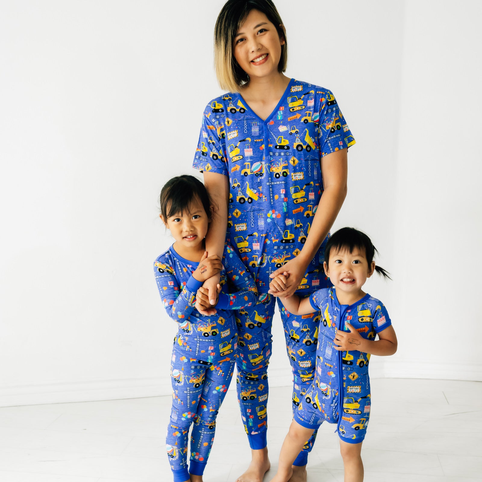 Mom with her two children wearing matching Birthday Builder pajamas. Mom is wearing women's Birthday Builders women's pants paired with a women's top. Children are wearing Birthday Builders pjs in two piece and zippy styles.