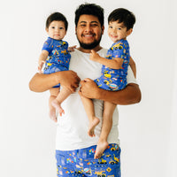 Dad with his two children wearing matching Birthday Builder pajamas. Dad is wearing men's Birthday Builders men's pants paired with a bright white men's top. Children are wearing Birthday Builders pjs in two piece and zippy styles.