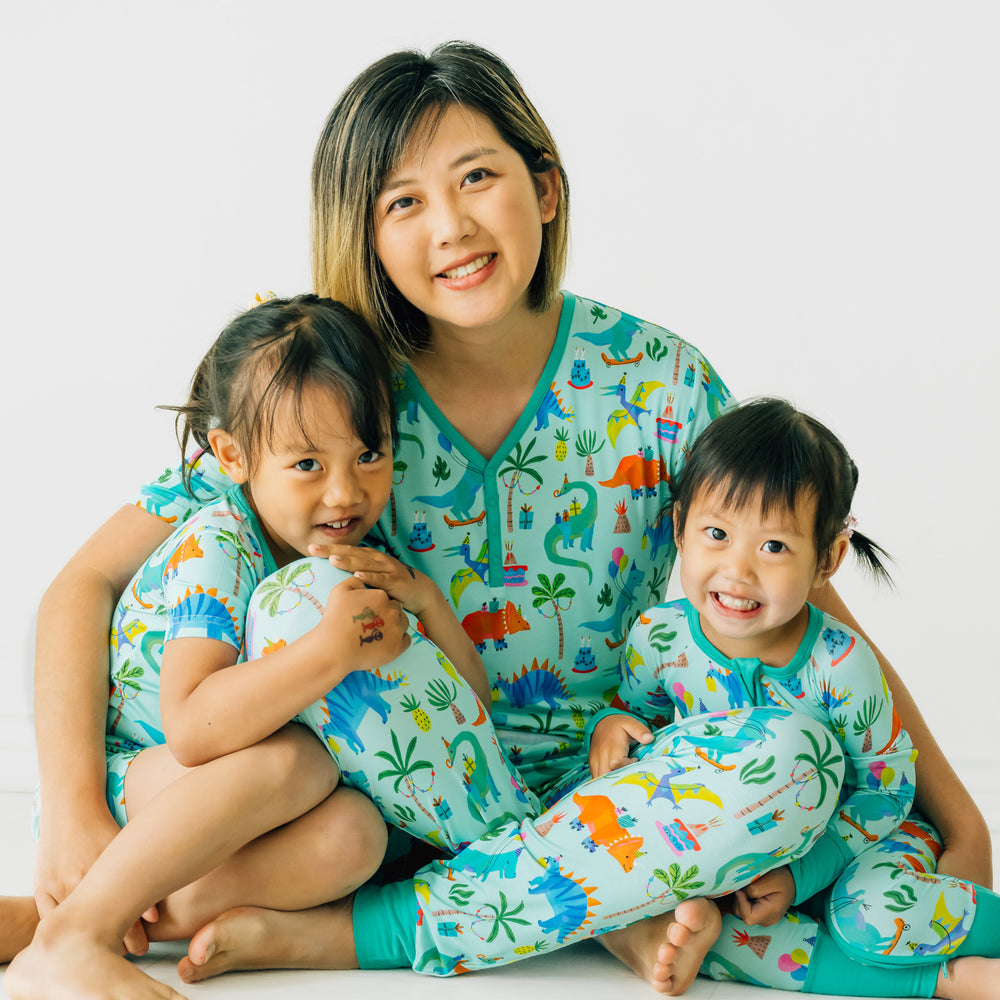 Woman wearing a Prehistoric Party women's short sleeve pj top and matching women's pj pants. Her two children are wearing matching zippy and two piece short sleeve and shorts pj sets