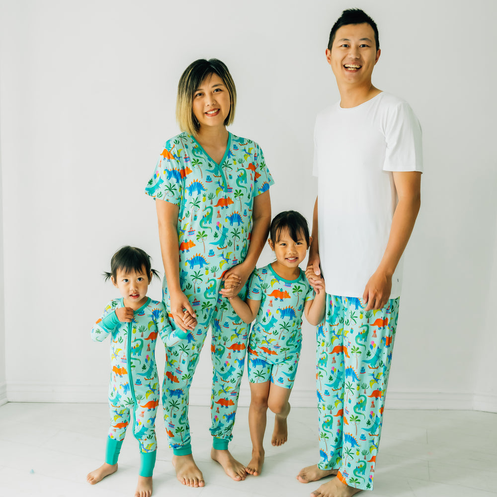 Alternate family of four wearing Prehistoric Party pjs. Dad is wearing a men's bright white pj top and Prehistoric Party men's pj pants. Mom is wearing women's Prehistoric Party women's pj top and pj pants. Their children are wearing matching Prehistoric Party pjs in zippy and two piece styles
