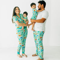 Family of four wearing Prehistoric Party pjs. Dad is wearing a men's bright white pj top and Prehistoric Party men's pj pants. Mom is wearing women's Prehistoric Party women's pj top and pj pants. Their children are wearing matching Prehistoric Party pjs in zippy and two piece styles