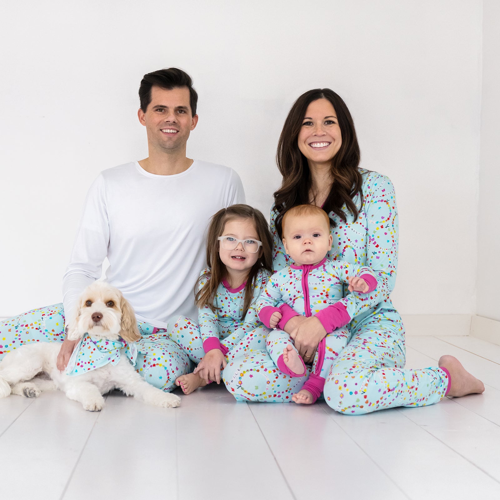 Image of a family of four with their dog wearing matching Friends Forever pjs. Mom and Dad are wearing men's and women's tops and bottoms in Friends Forever print. Kids are wearing Friends Forever pjs in two piece and zippy styles.