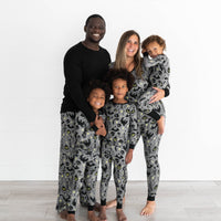 Family in the Gray Glowing Ghouls print. Male model on the left is in the Gray Glowing Ghouls Men's Pajama Pants & Black Men's Pajama Top. Two boys in the front are wearing the Gray Glowing Ghouls Two-piece Pajama Set. Female model is holding child in the Gray Glowing Ghouls Zippy, while wearing the Gray Glowing Ghouls Women's Pajama Pants & Tops