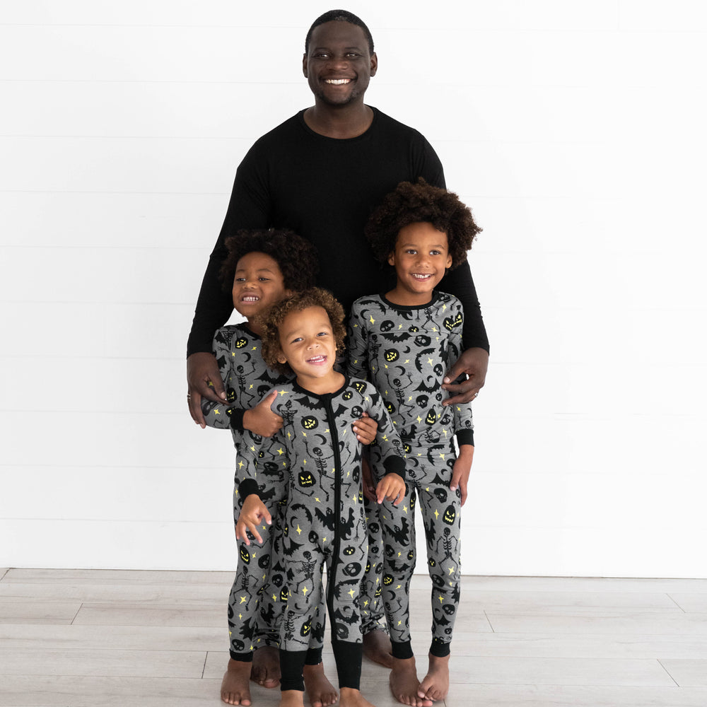 Male model in the Solid Black Men's Pajama Top and two boys are in the Gray Glowing Ghouls Two-piece Pajama Set. Boy in the middle is wearing the Gray Glowing Ghouls Zippy