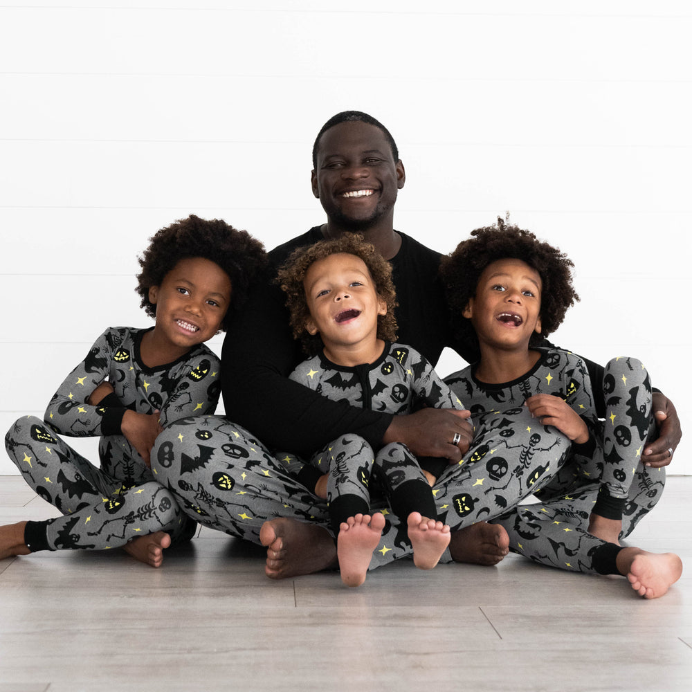 Family in the Gray Glowing Ghouls Print. Boys on the right and left are in the Gray Glowing Ghouls Two-piece Pajama Pants. Boy in the middle is in the Gray Glowing Ghouls Zippy and father is in the Gray Glowing Ghouls Men's Pajama Pants & Black Men's Pajama Top