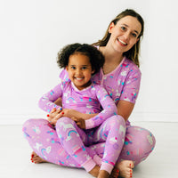 Mother and daughter sitting together wearing matching Magical Birthday pjs. Mom is wearing women's Magical Birthday pj top and matching pj pants. Child is wearing magical birthday two piece pj set