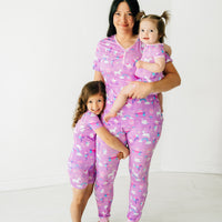 Mother and two daughters posing together wearing matching Magical Birthday pjs. Mom is wearing women's Magical Birthday pj top and matching pj pants. Children are wearing magical birthday two piece pj set and shorty zippy