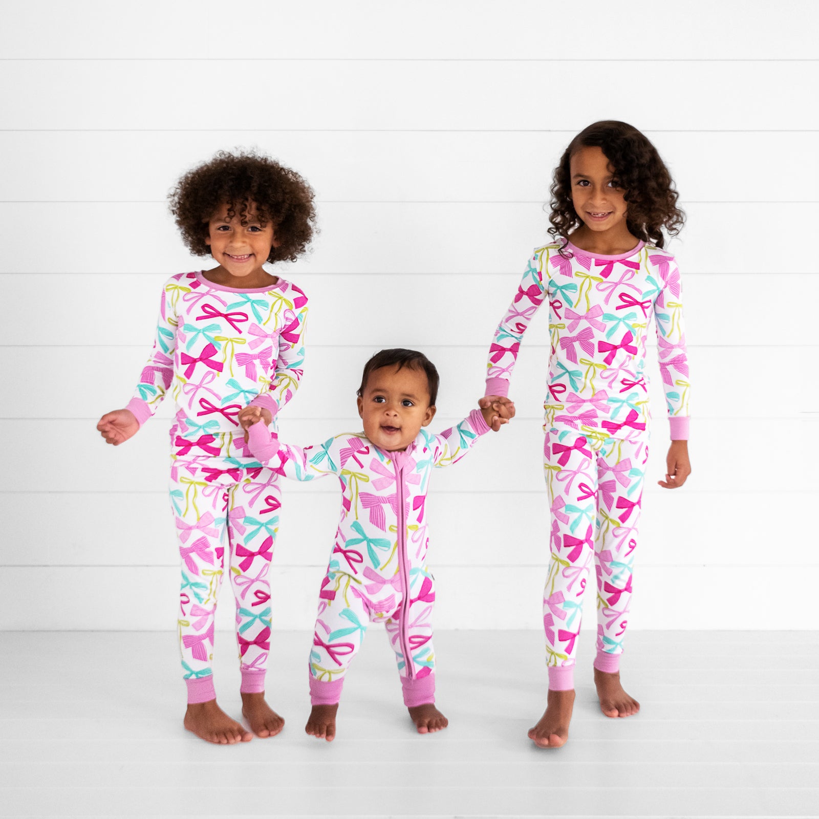 three children holding hands wearing matching Ribbons and Bows pj sets in two piece and zippies