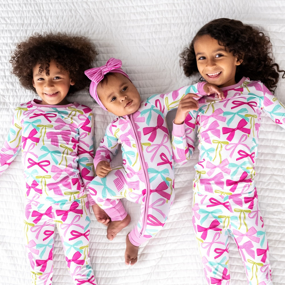 three children laying on a bed wearing matching Ribbons and Bows pj sets in two piece and zippies