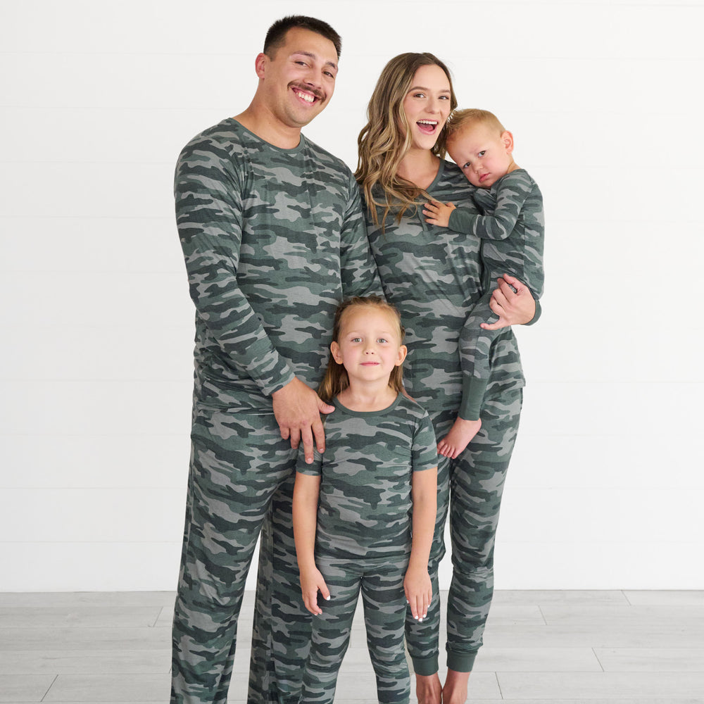 Male model on the left is wearing the Vintage Camo Men's Pajama Top & Pants, girl in the middle is wearing the vintage camo short-sleeve pajama set. Female model is wearing the Vintage Camo Women's Pajama Top & Pants, while holding boy in the vintage camo zippy