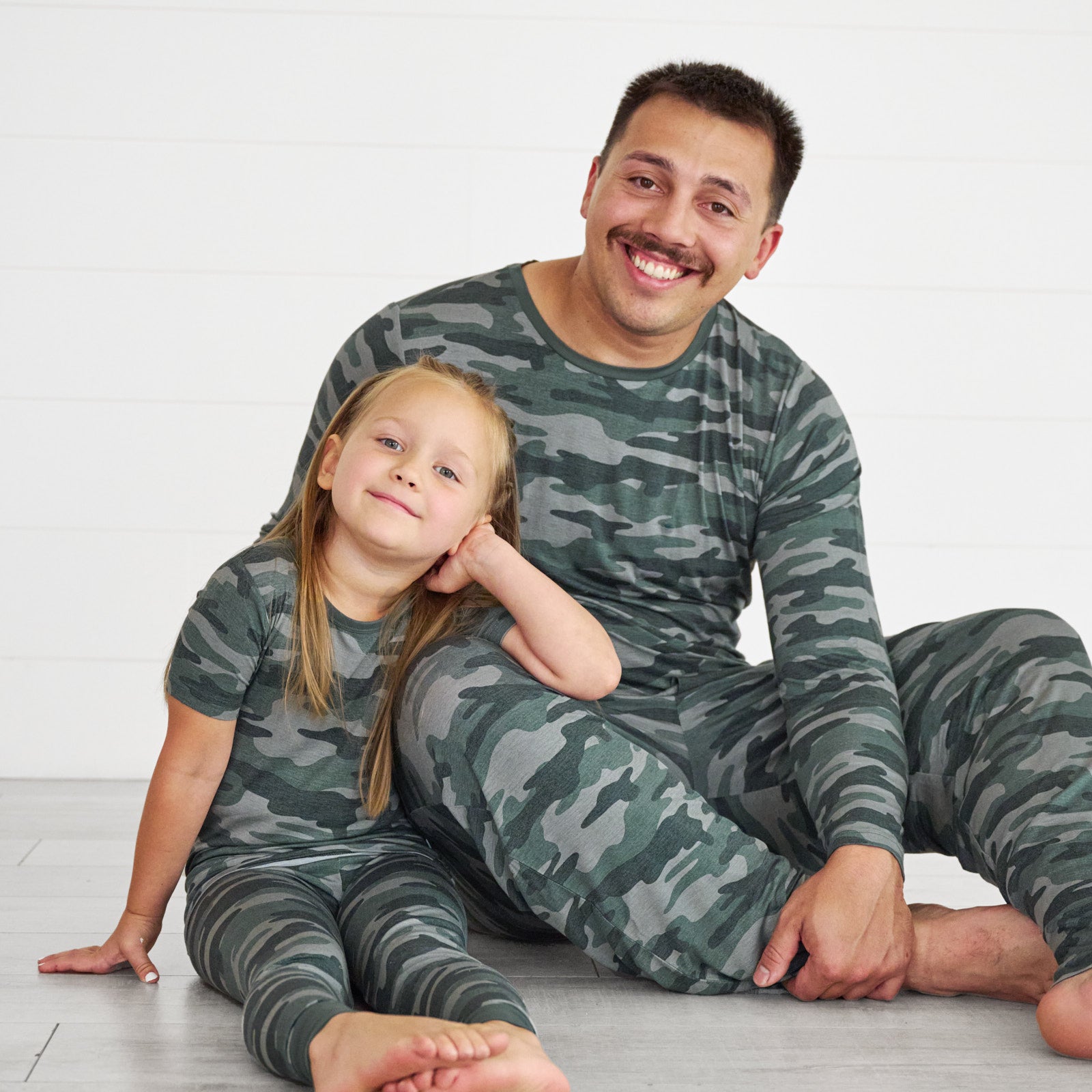 Girl on the left is wearing the Vintage Camo Short Sleeve Pajama Set and father on the right is in the Vintage Camo Men's Pajama Pants & Top