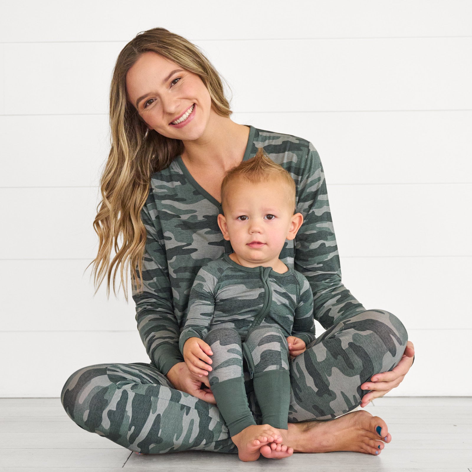 Female model wearing the Vintage Camo Women's Pajama Pants & Top, while holding baby in the Vintage Camo Zippy