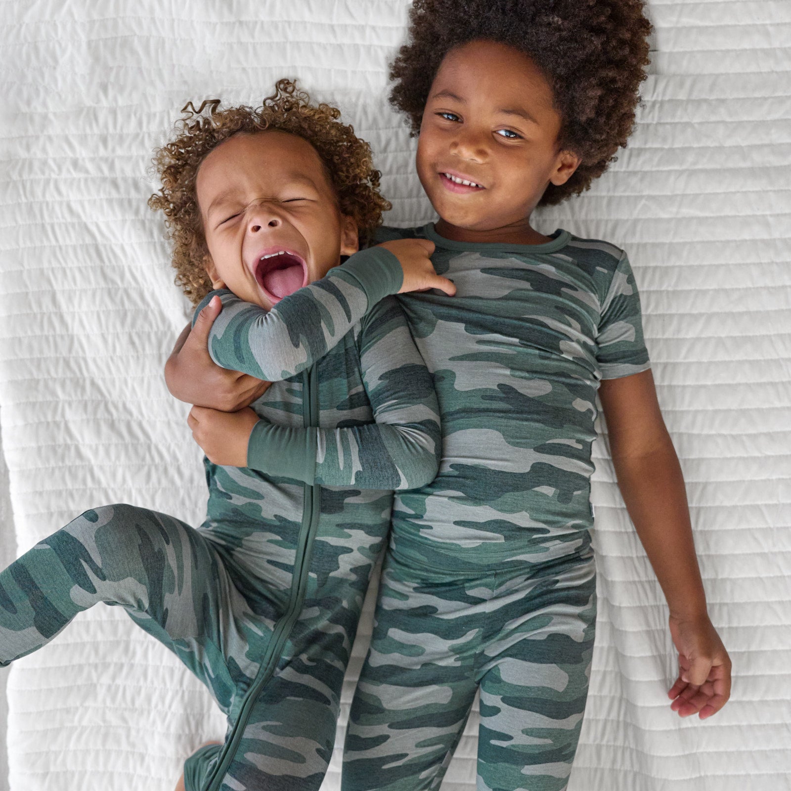 Top view image of two brothers laying down. The boy on the left is in the Vintage Camo Zippy and boy right is in the Vintage Camo Short-sleeve Two Piece Pajama Set