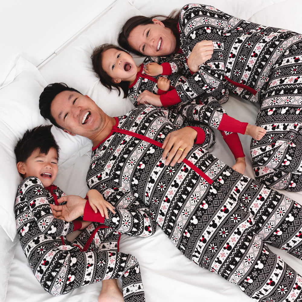 Family of four laying on a bed wearing matching Mickey Fair Isle zippies in men's, women's, and children's styles