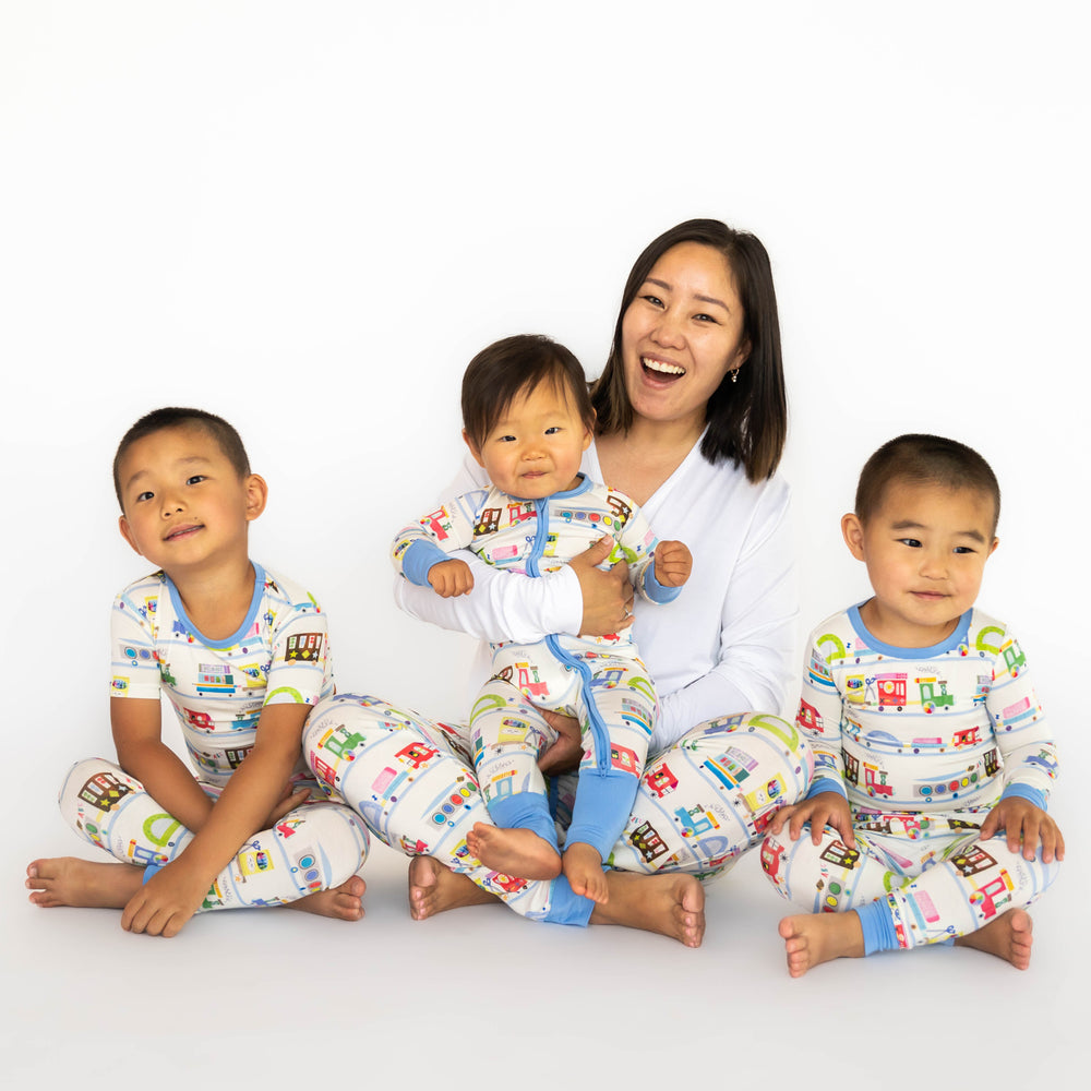 Mother and three children sitting, while wearing the Education Express Pajamas. First child on the left is wearing the Education Express Two-Piece Short Sleeve Pajama Set. Baby is wearing the Education Express Zippy and mother is wearing the Education Express Women's Pajama Pants. Child on the right is wearing the Education Express Two-Piece Pajama Set.