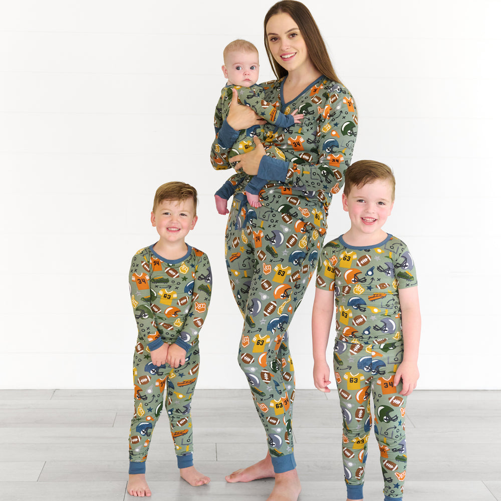 Boy on the left is wearing the touchdown-time-two-piece-pajama-set, female model in the middle is wearing the touchdown-time-womens-pajama-pants top, while holding baby in the touchdown-time-zippy. Boy on the right is the touchdown-time-two-piece-short-sleeve-pajama-set