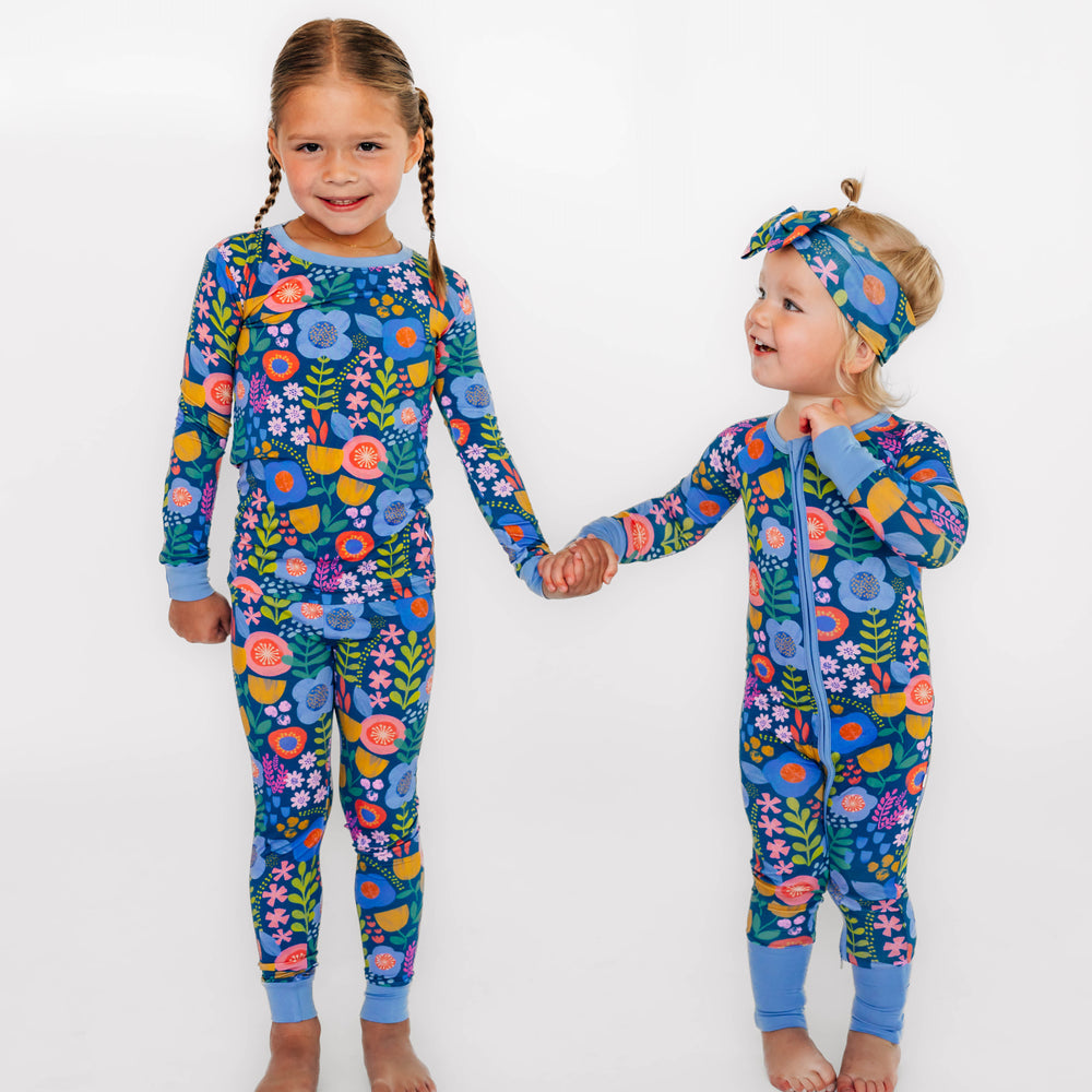 Two girls wearing the Folk Floral print. Girl on the left is wearing the Folk Floral Two-Piece Pajama Set and girl on the right is wearing the Folk Floral Zippy with Folk Floral Luxe Bow Headband