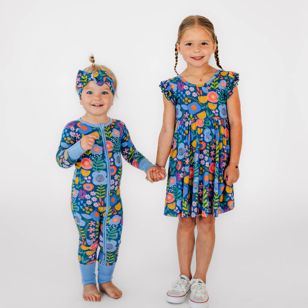 Two girls standing in the Folk Floral Print. Girl on the left is wearing the Folk Floral Zippy & Folk Floral Luxe Bow Headband. Girl on the right is wearing the Folk Floral Flutter Twirl Dress