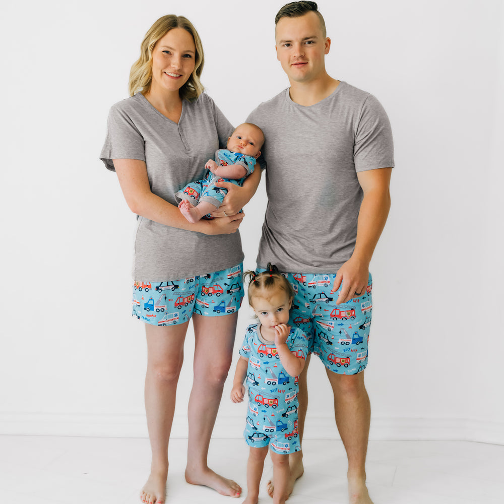 Family of four wearing matching To The Rescue printed pajamas. Mom is wearing women's To the Rescue pj shorts and coordinating heather gray women's pajama top. Dad is wearing men's To the Rescue pj shorts and coordinating heather gray men's pajama top. Children are wearing To The Rescue zippy and two piece pajama sets