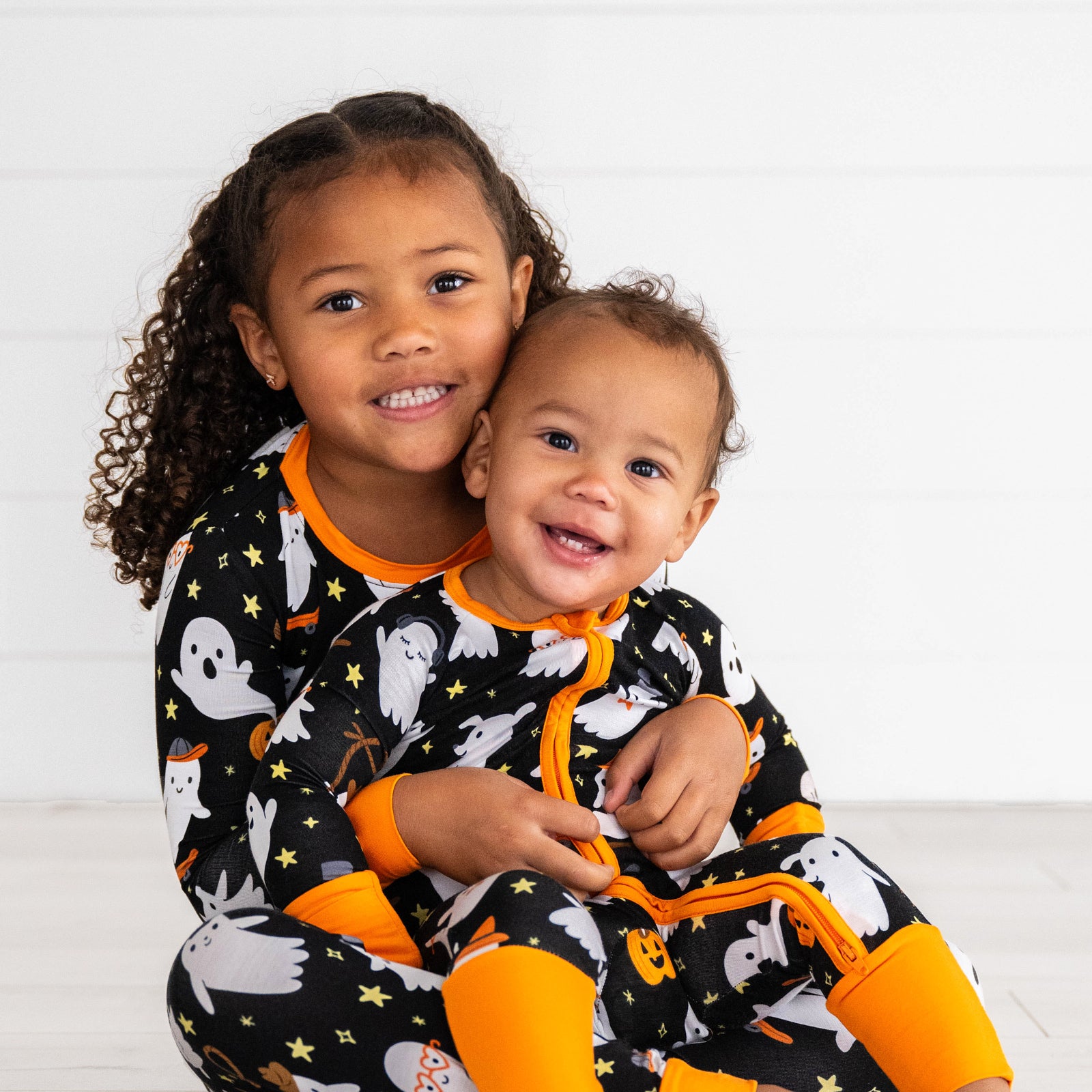 Siblings in the Friendly Ghosts print. Girl is holding her younger sibling in the Friendly Ghosts Two-piece Pajama Set. Baby is wearing the Friendly Ghosts Zippy