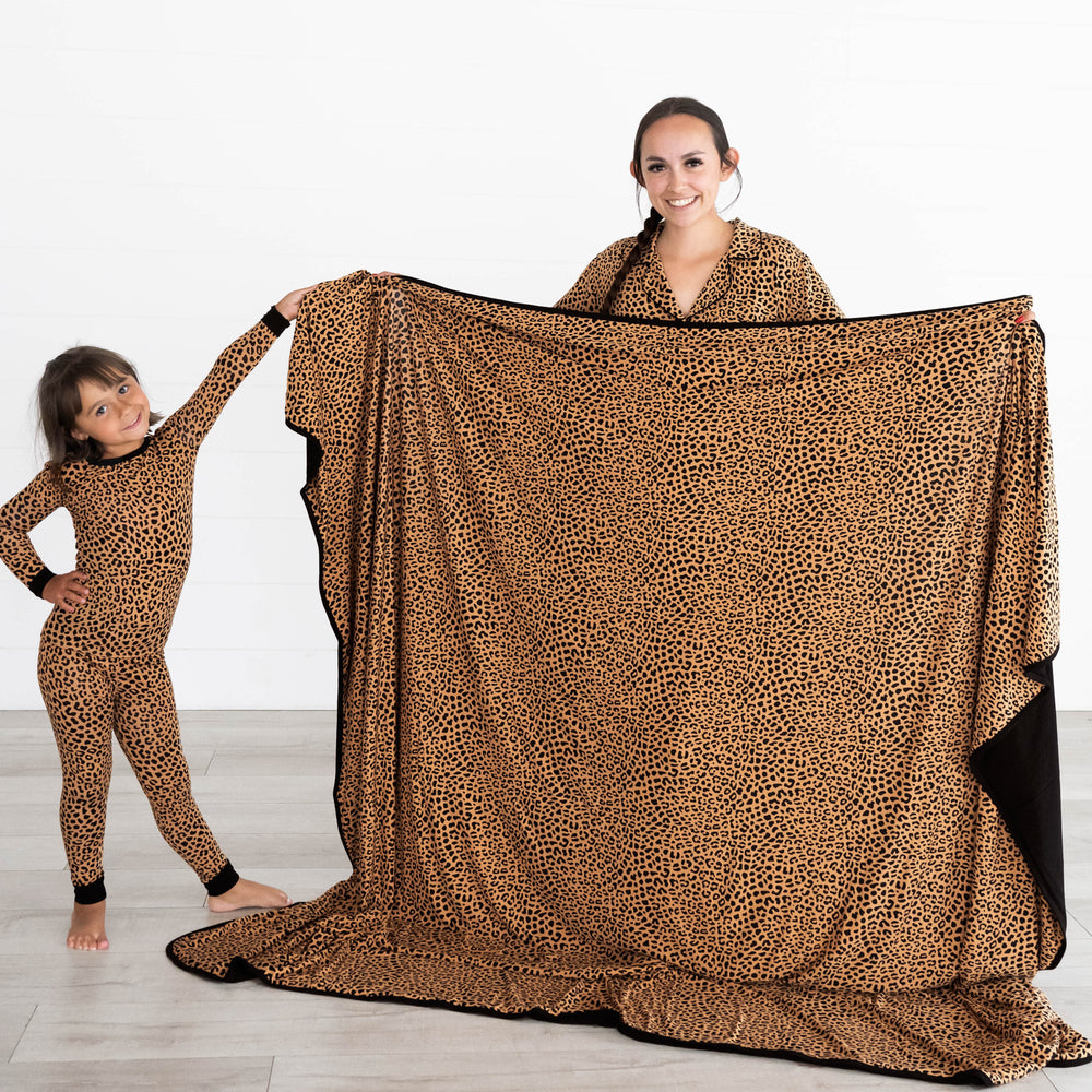 Girl on the left is in the Classic Leopard Two-piece Pajama Set while holding up the Classic Leopard Oversized Cloud Blanket® with mother