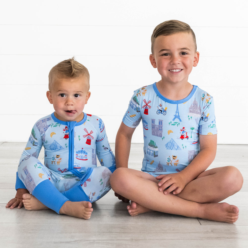 Boy on the left is wearing the Blue Weekend in Paris Zippy and boy on the left is sitting while wearing the Blue Weekend in Paris Short-sleeve & Shorts Pajama Set