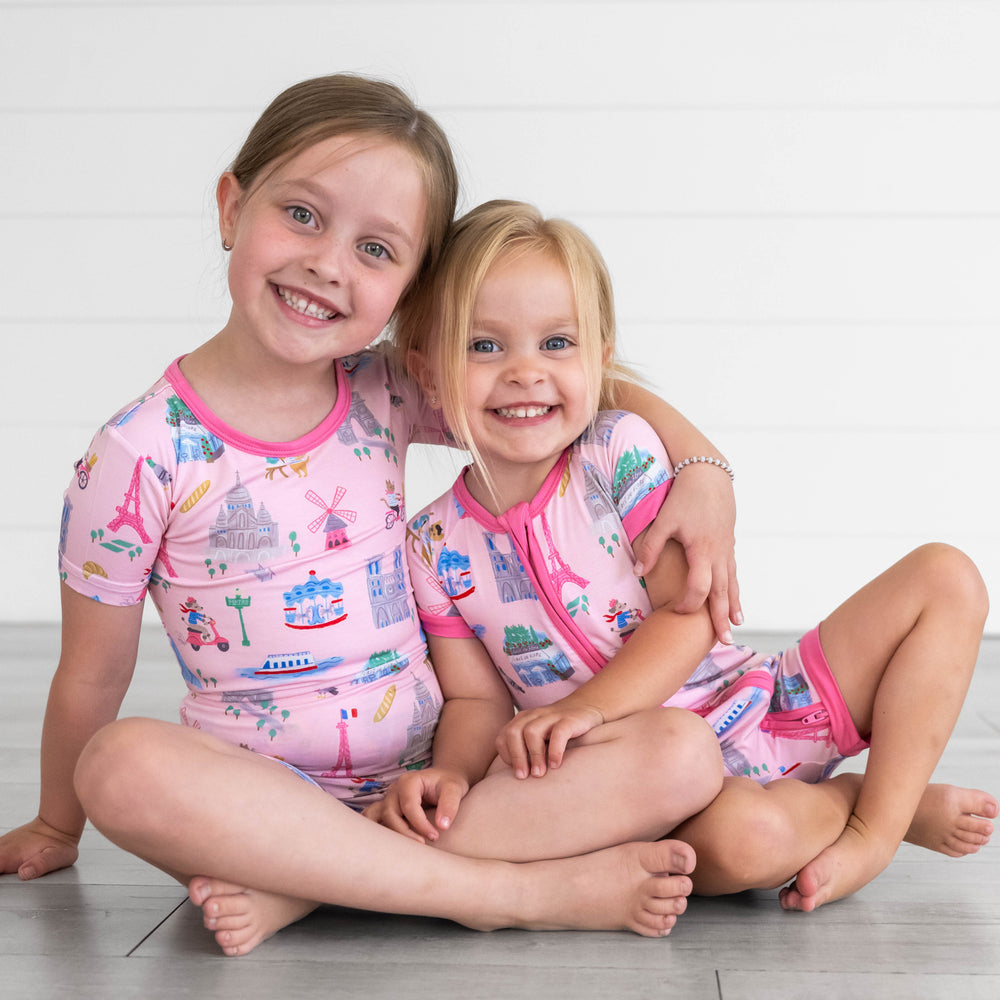 Girl on the left is wearing the Pink Weekend in Paris Short-sleeve & Shorts Pajama Set and girl on the right is in the Pink Weekend in Paris Shorty Zippy