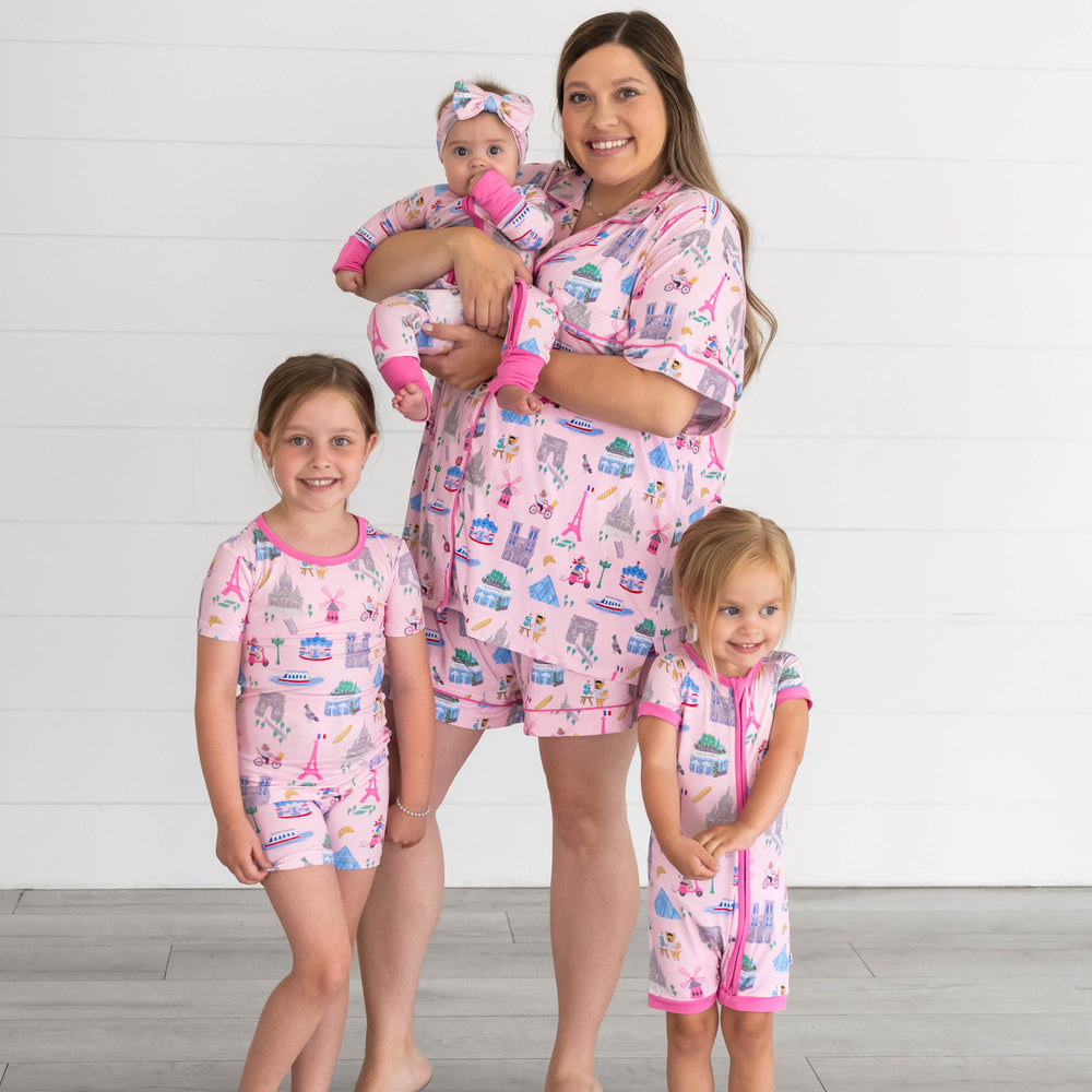 Family in the Pink Weekend in Paris print. Girl on the left is in the Pink Weekend in Paris Short-sleeve & Shorts Pajama Set. Baby being held by mother is in the Pink Weekend in Paris Zippy and mother is the in Pink Weekend in Paris Women's Short-Sleeve Pajama Set. Girl on the right is in the Pink Weekend in Paris Shorty Zippy