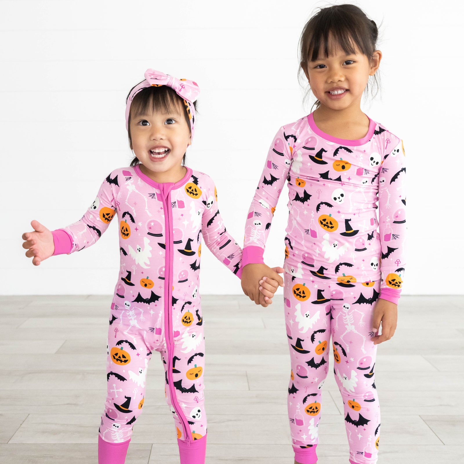 Girl on the left is in the Pink Glowing Ghouls Zippy and girl on the right is in the Pink Glowing Ghouls Two-Piece Pajama Set