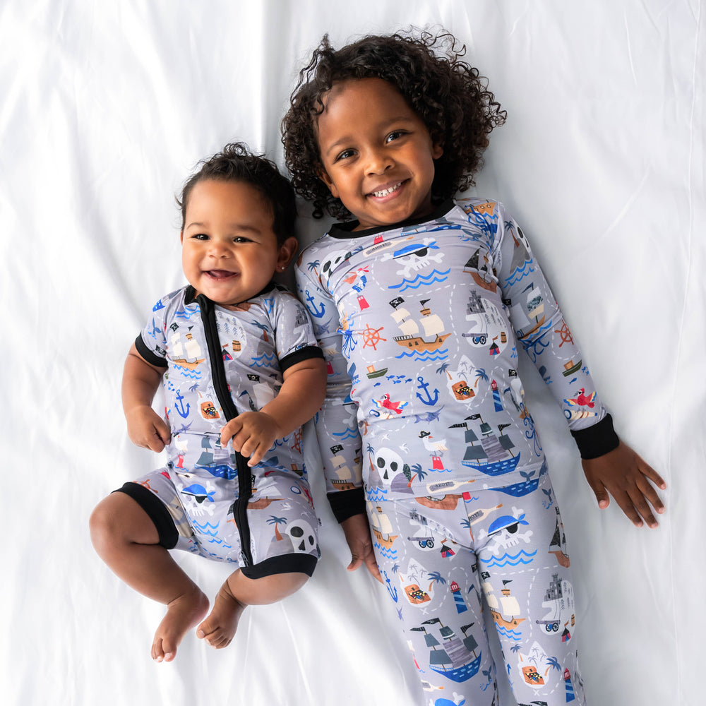 Two children wearing the Pirate's Map print. Baby on the left is wearing the Pirate's Map Shorty Zippy and child on the right is wearing the Pirate's Map Pajama Set
