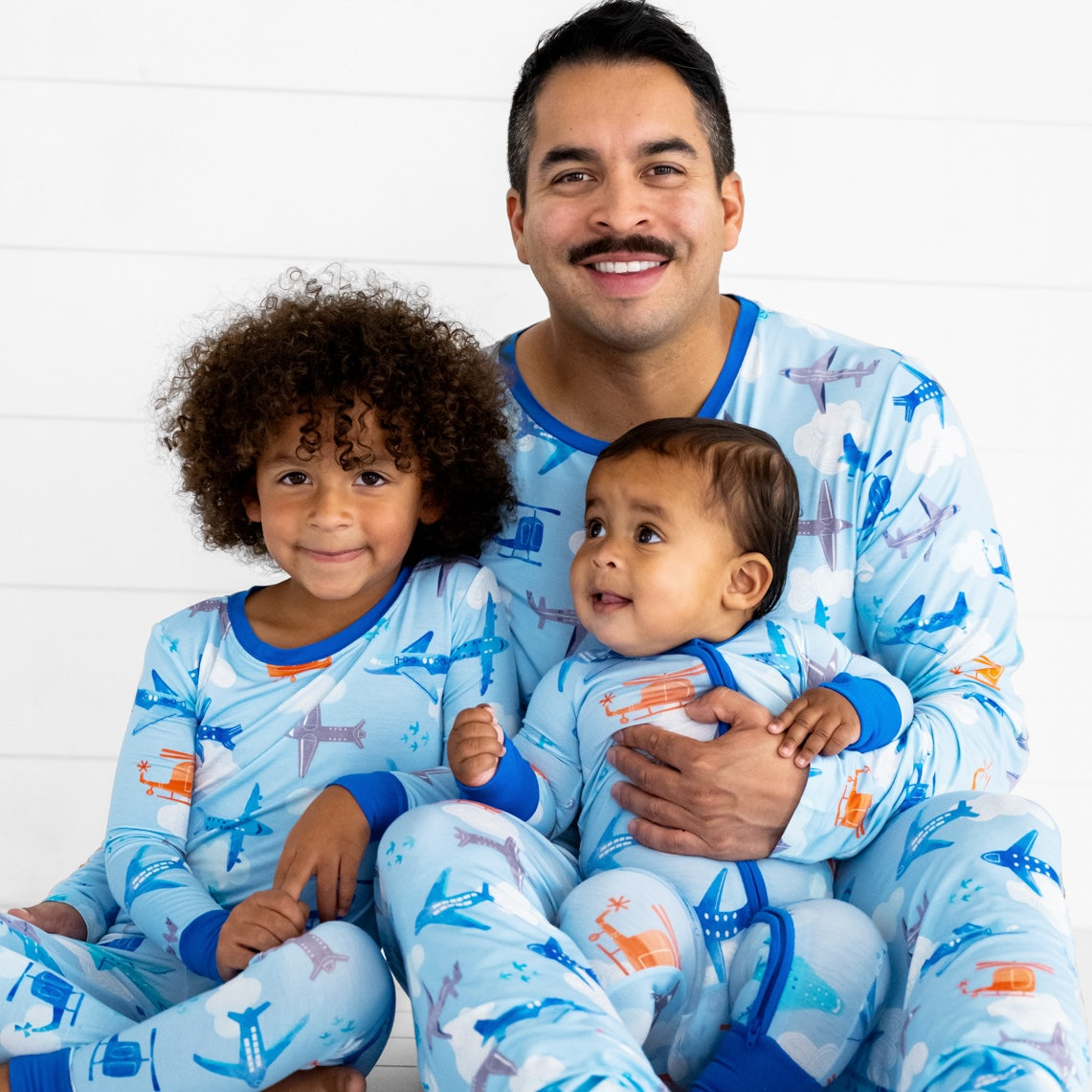 Father and his two children wearing matching Lets Fly pjs in men's and children's two piece and zippy styles