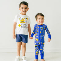 Two children wearing coordinating Birthday Builders outfits. Child is wearing a Birthday Builders construction graphic tee paired with vintage navy shorts. His sibling is wearing a Birthday Builders zippy