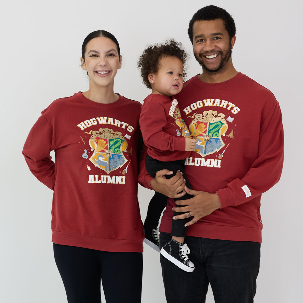 Woman and man holding child wearing Hogwarts Alumni Sweatshirt